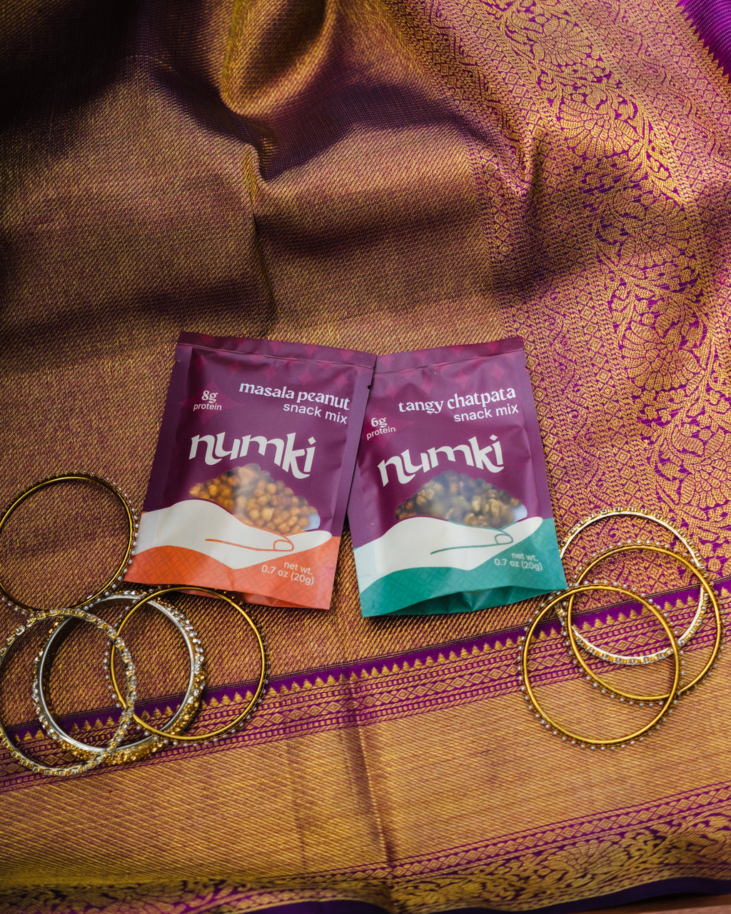 Two Numki snack mix packets on a sari with gold bangles.