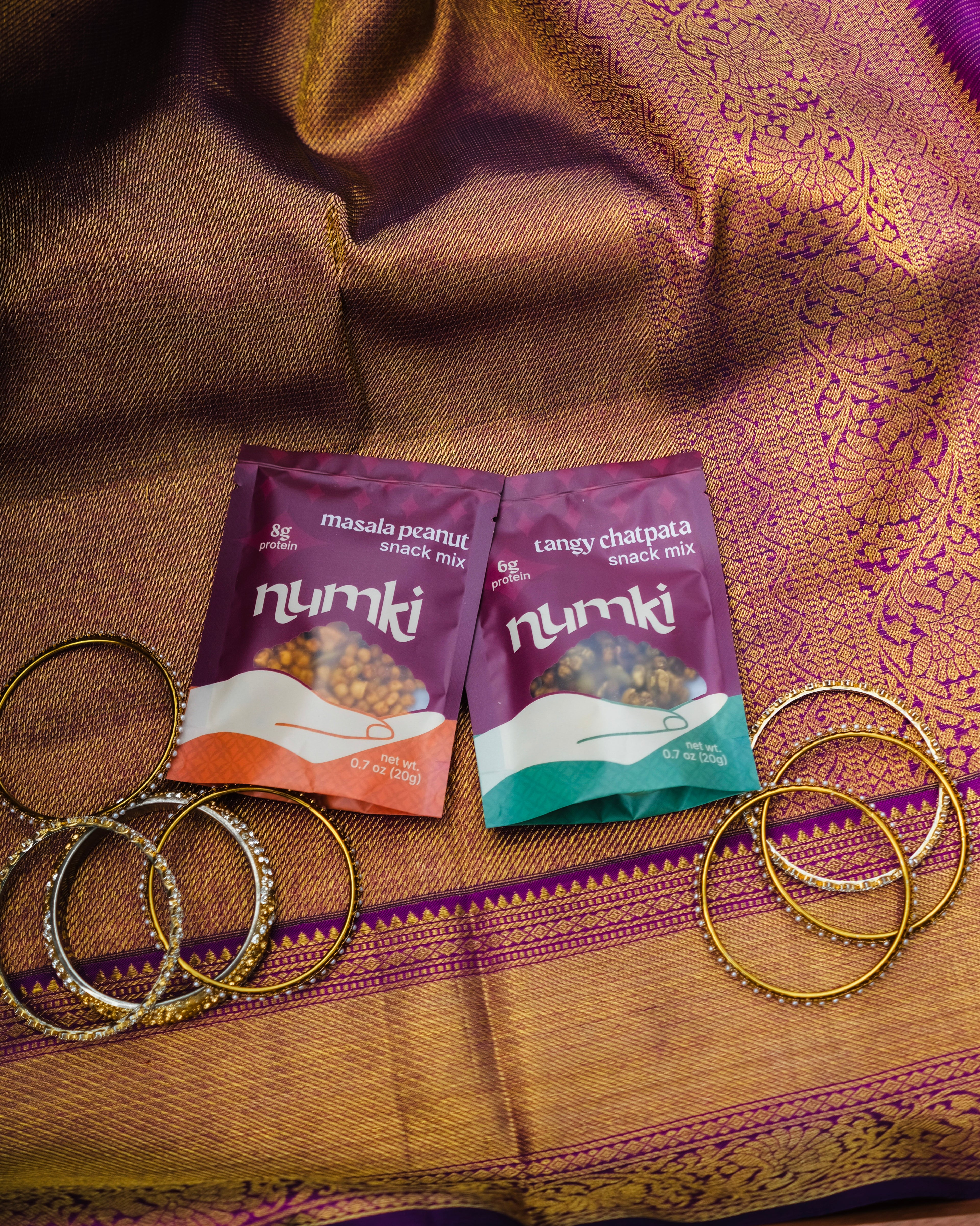 Two Numki snack mix packets on a sari with gold bangles.